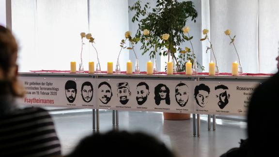 Tisch mit weißen Kerzen und Rosen über einem Banner mit den Bildern der Opfer