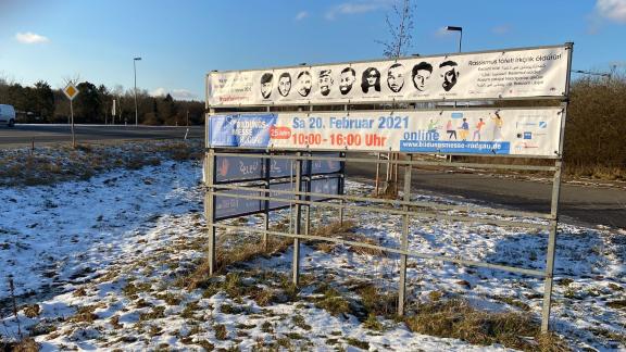 Ein Banner schmales Banner zum Gedenken an die neun Opfer des Anschlags von Hanau ist am Ortseingang auf einer Ausstellungsfläche gespannt. Im Vordergrund liegt Schnee. 